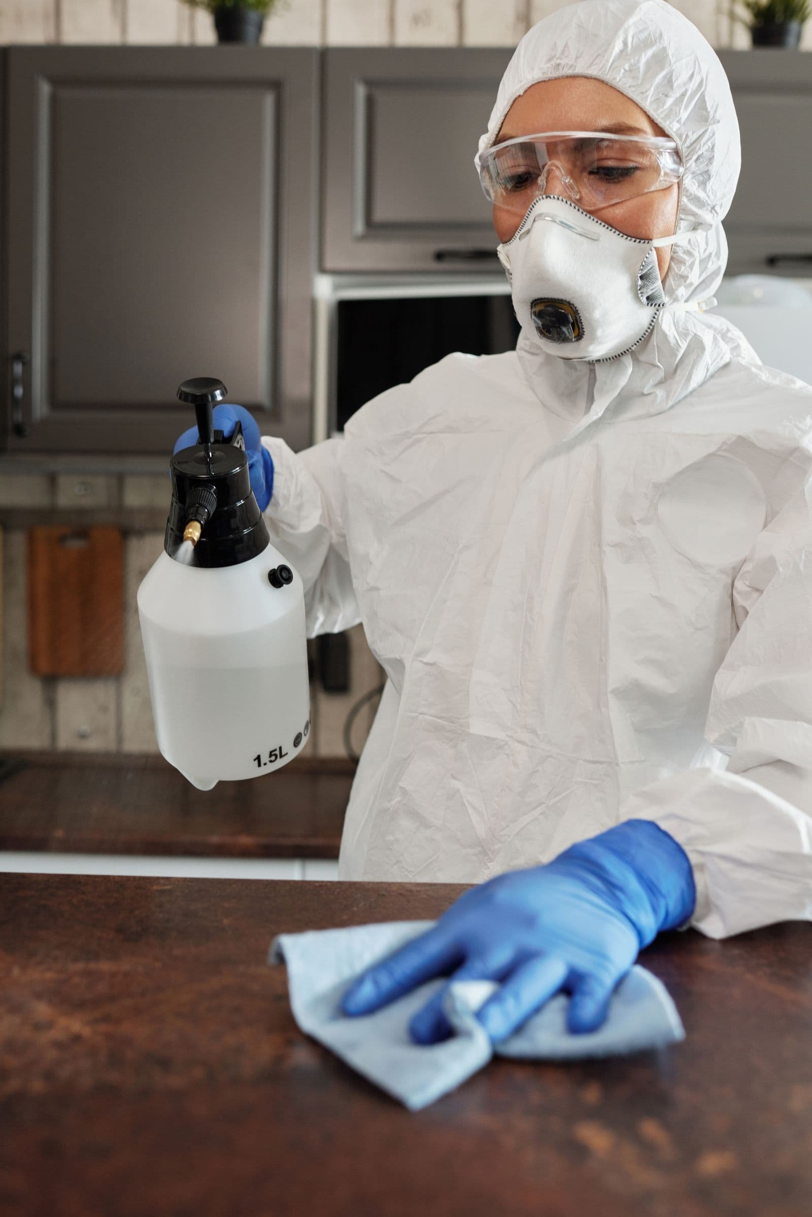 Opérateur en combinaison intégrale pulvérisant un produit désinfectant sur une surface